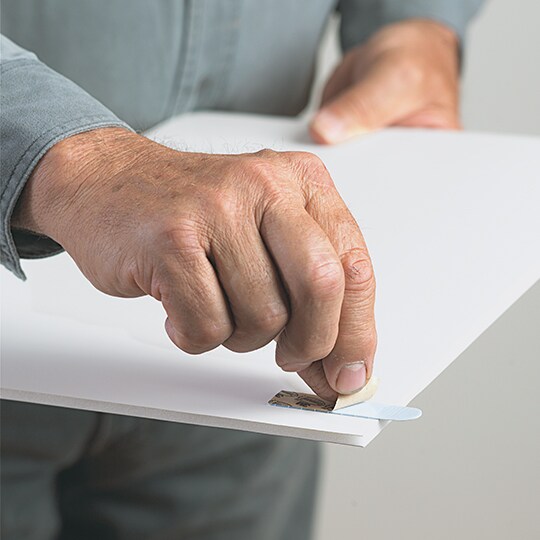 Person applying Command Picture Hanging Strip on the back of a photo frame